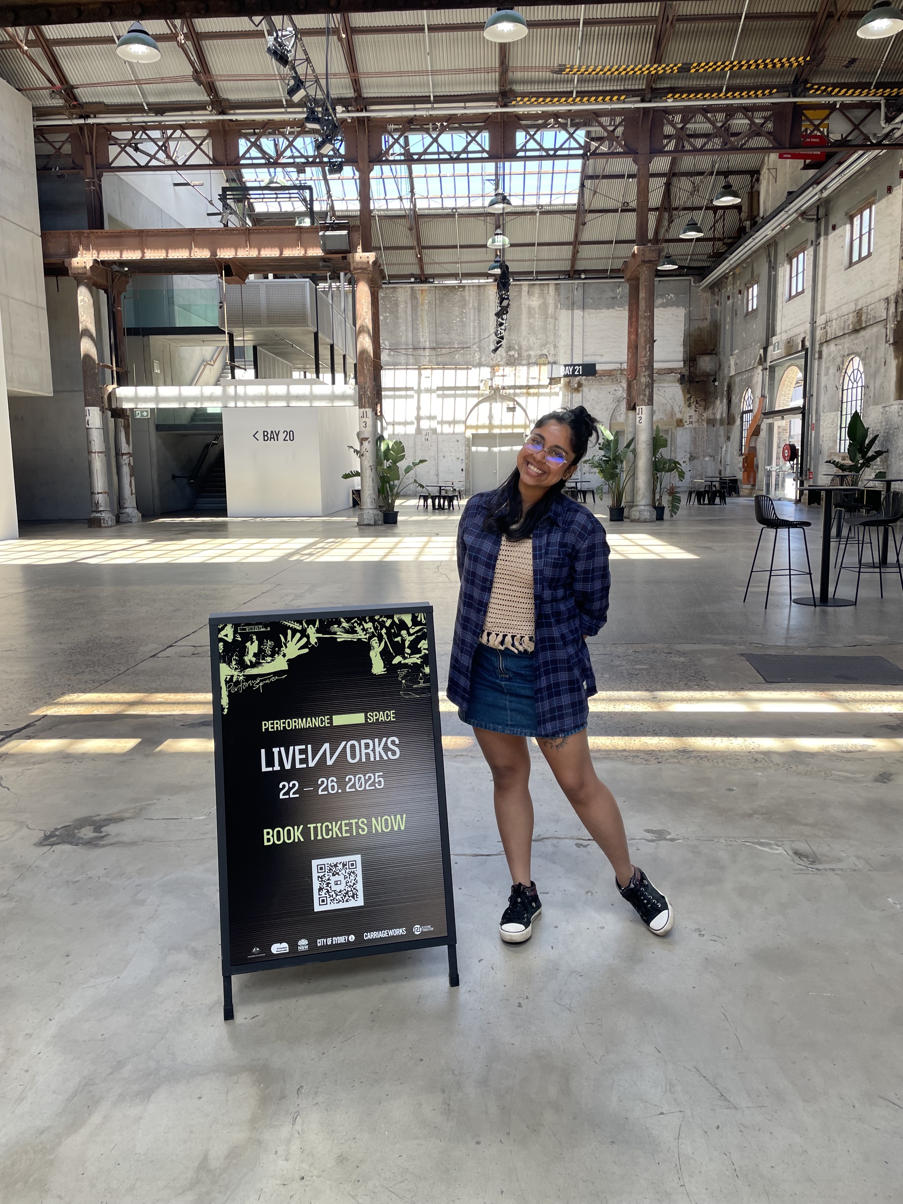 Akriti Banerjee standing next to Liveworks A-frame in Carriageworks foyer.